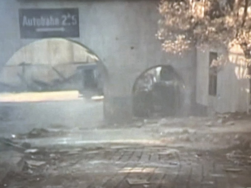 A view of a dusty road leading through an arched tunnel with a sign that reads 'Autopista 2:5' in the background, surrounded by debris and vegetation.