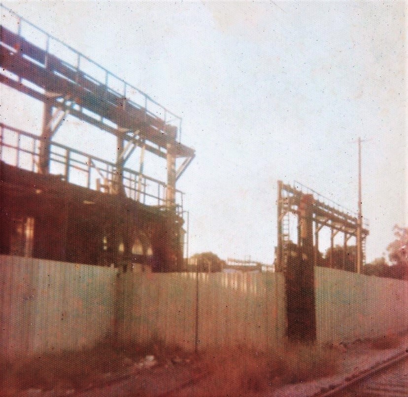 Construction site with industrial structures and a surrounding fence, under a clear sky.