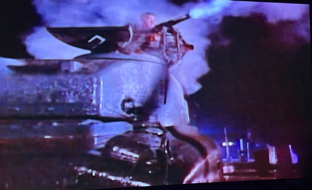 A tank with a person operating the turret, emitting smoke and firing a weapon in a dramatic scene.