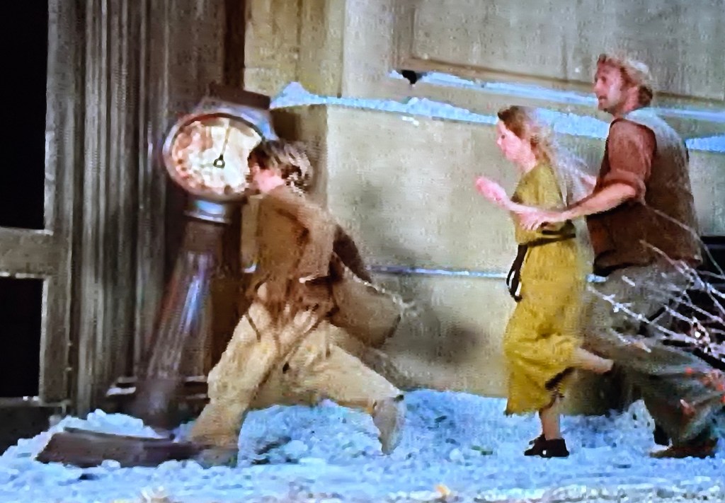 A scene featuring three characters running past an ornate clock, surrounded by snow and an indoor setting.