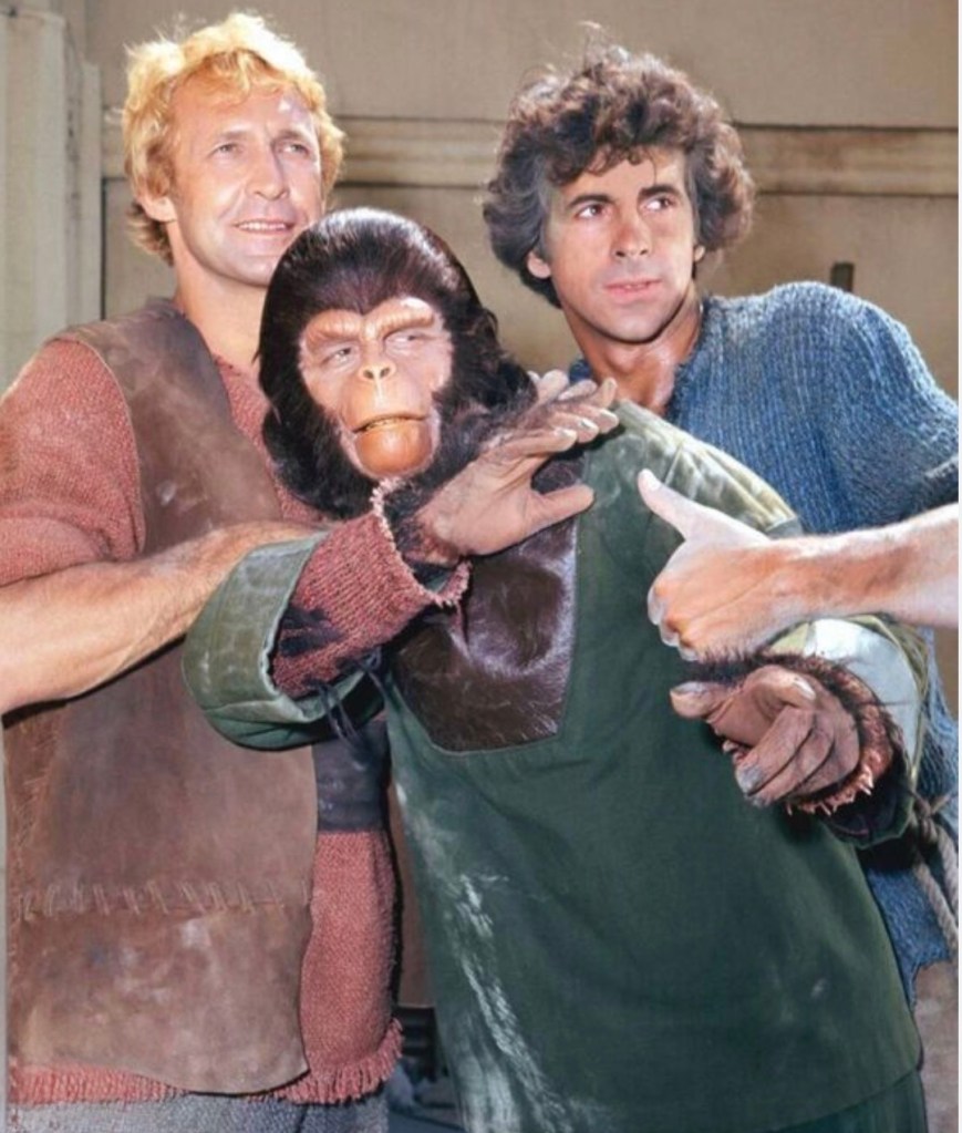 A group of three characters posing together, one is wearing a realistic ape costume, while the others are dressed in distinctive, historical-style clothing.