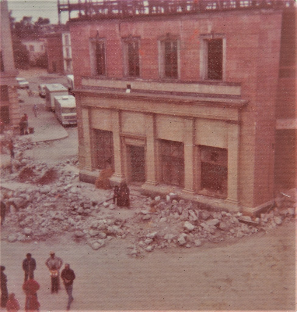 A historic building under renovation, with construction debris scattered in front and workers present in the area.