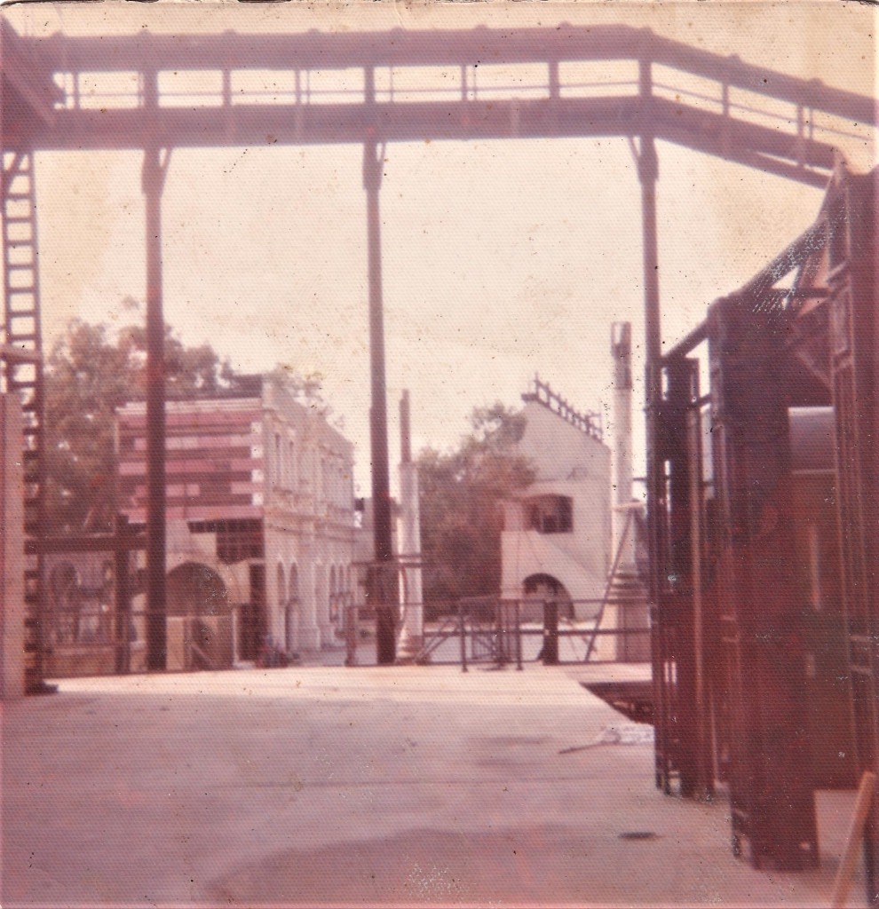 Historical film set featuring empty streets, a bridge structure overhead, and vintage-style buildings in the background.