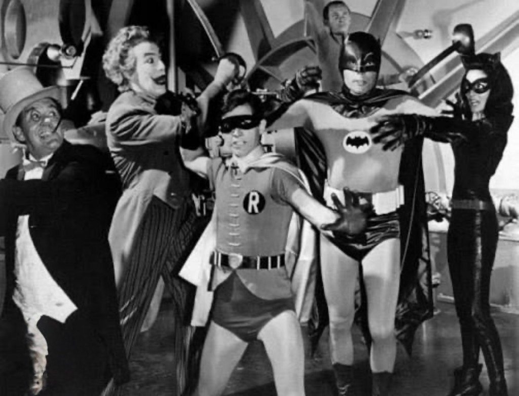 A vintage black and white scene featuring iconic characters including Batman, Robin, Catwoman, and the Penguin in a playful standoff.