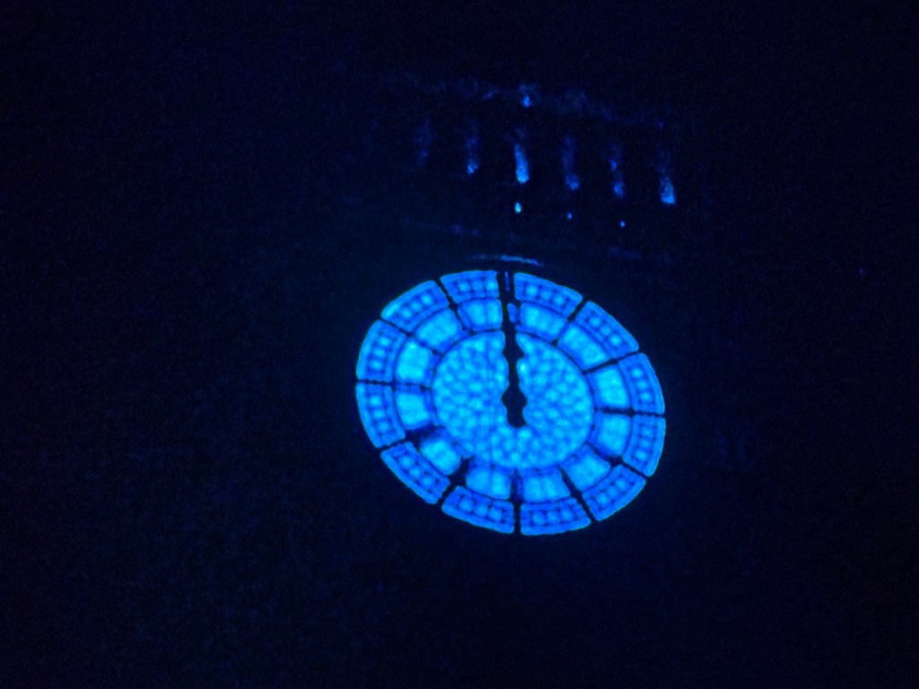 A close-up view of a blue illuminated clock face against a dark background.