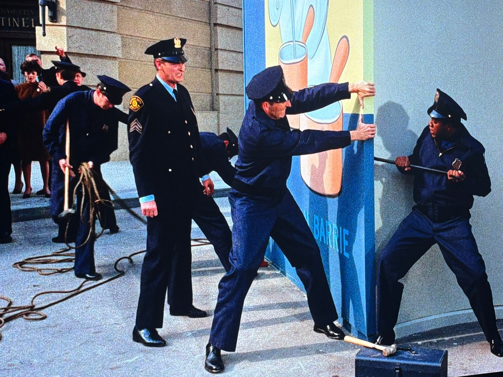 A group of police officers working together to move a large advertisement while an onlooking crowd watches.