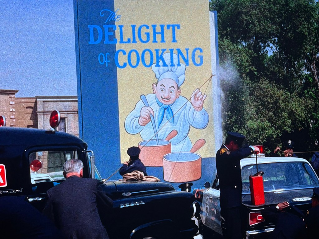 A colorful mural titled 'The Delight of Cooking' featuring a cheerful chef, while police and bystanders respond to an emergency situation with fire trucks and a vintage car.
