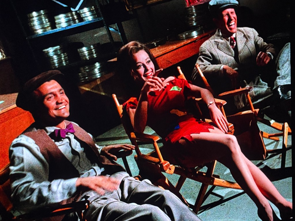 Three people sitting on director's chairs in a studio, smiling and enjoying a moment together.