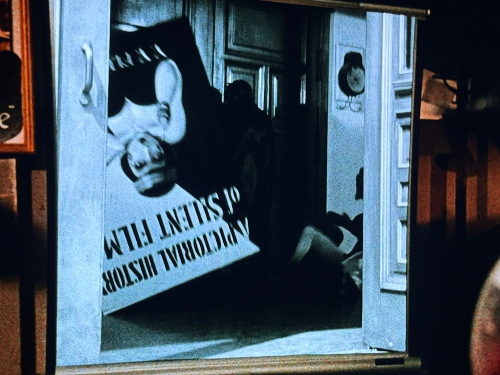 A vintage poster for a silent film displayed in a doorway with a partially visible figure in the background.