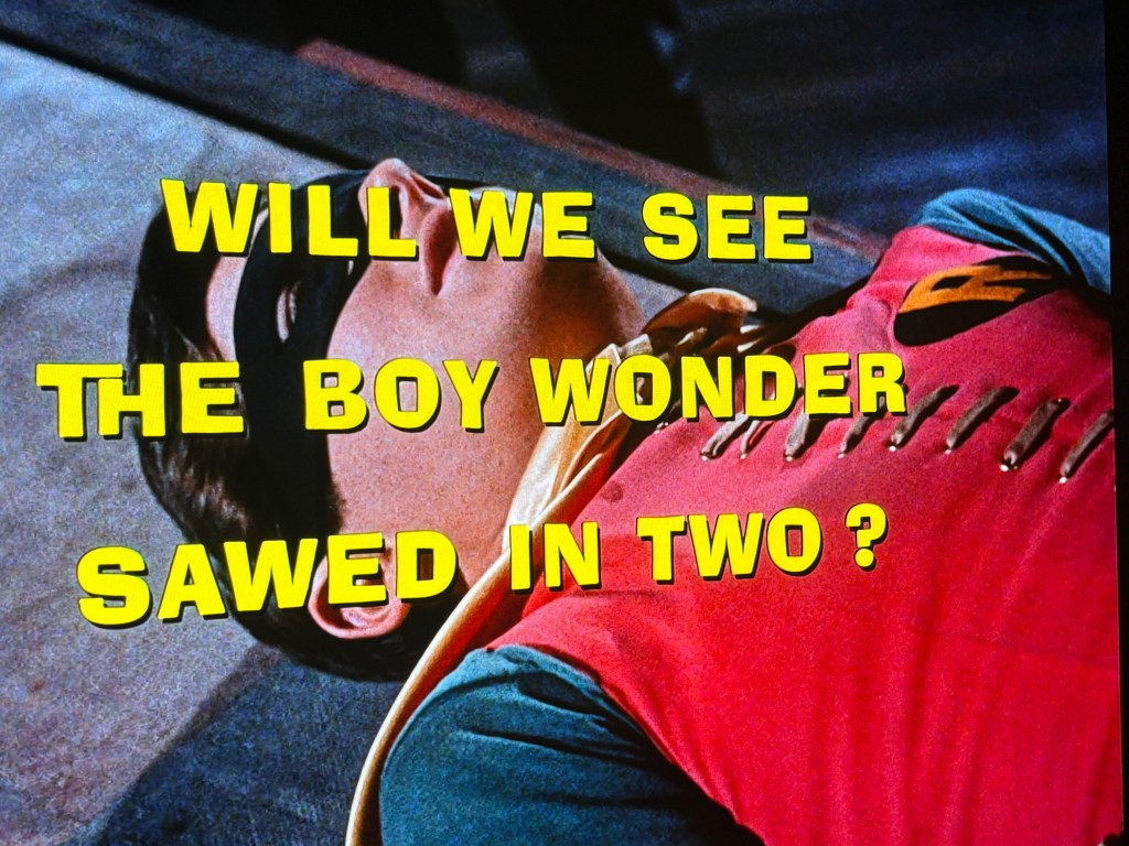 Image features bold text that reads 'WILL WE SEE THE BOY WONDER SAWED IN TWO?' over a scene showing a character lying down.