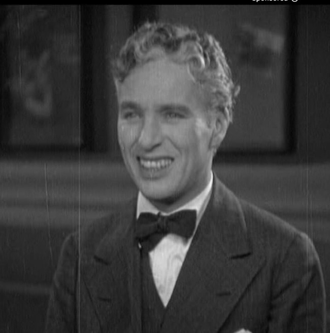 A smiling man with curly hair wearing a bow tie and a suit in a vintage black and white photo.