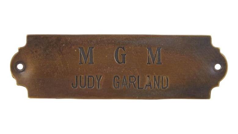 A vintage metal nameplate engraved with 'MGM' and 'JUDY GARLAND'.