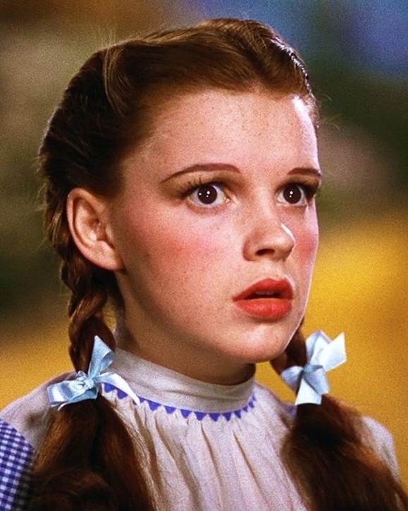 Close-up of a young girl with braided hair and blue bows, looking surprised or concerned.