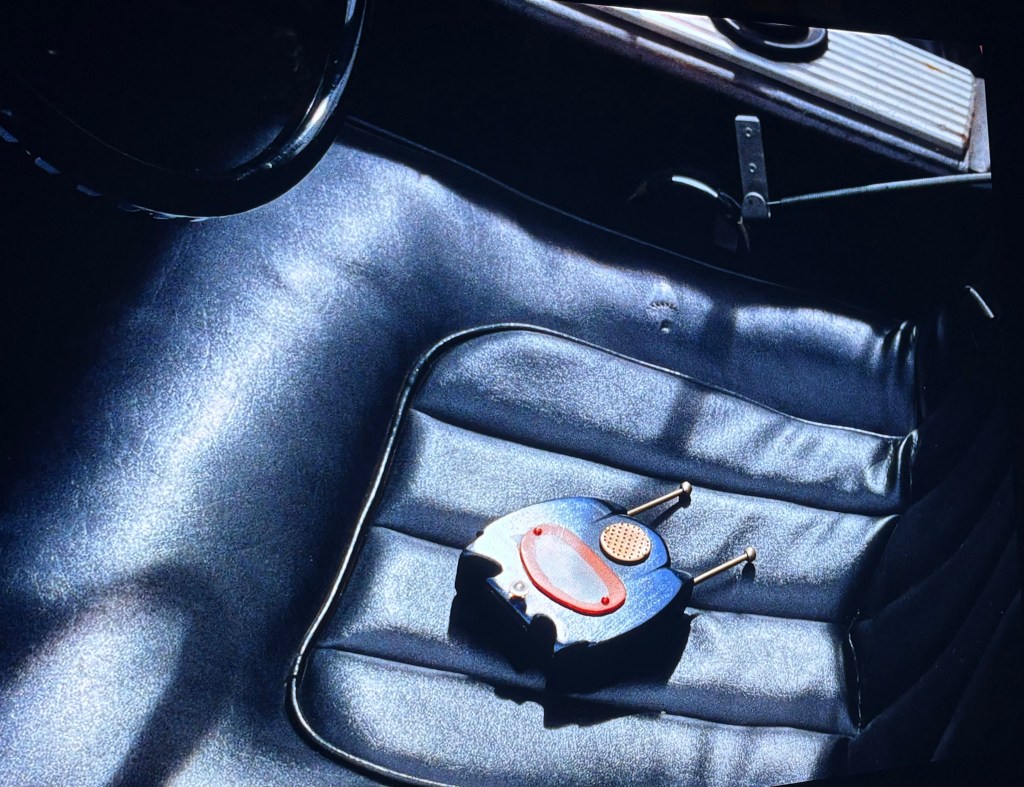A vintage radio device resting on a sleek black leather car seat, illuminated by sunlight.