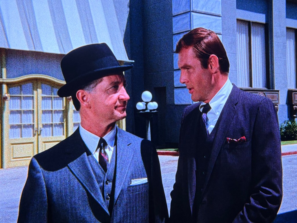 Two men in vintage attire engage in conversation outside a building with a striped awning, showcasing a stylized urban backdrop.