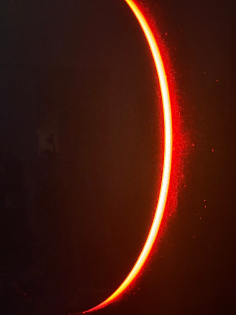 A glowing red arc emitting light against a dark background, possibly representing a light source or artistic effect.
