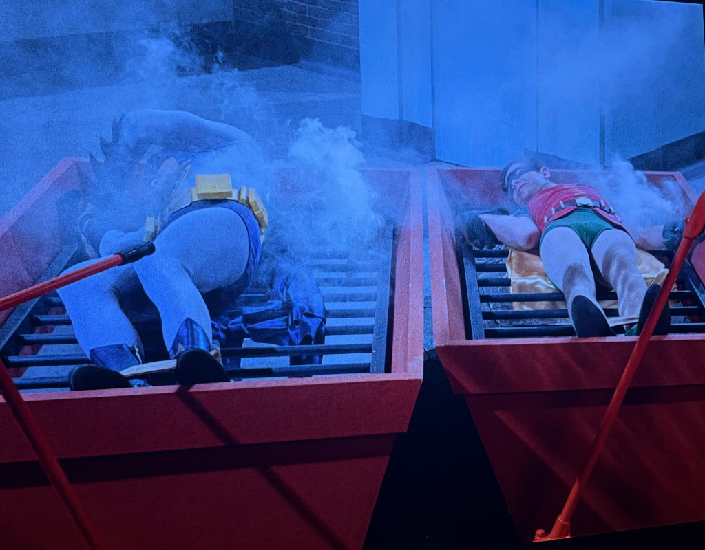 Batman and Robin lying on red platforms with steam rising around them, captured in a dramatic scene.
