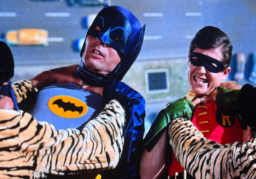 Batman and Robin being lifted by men in tiger-striped costumes in a colorful comic book scene.