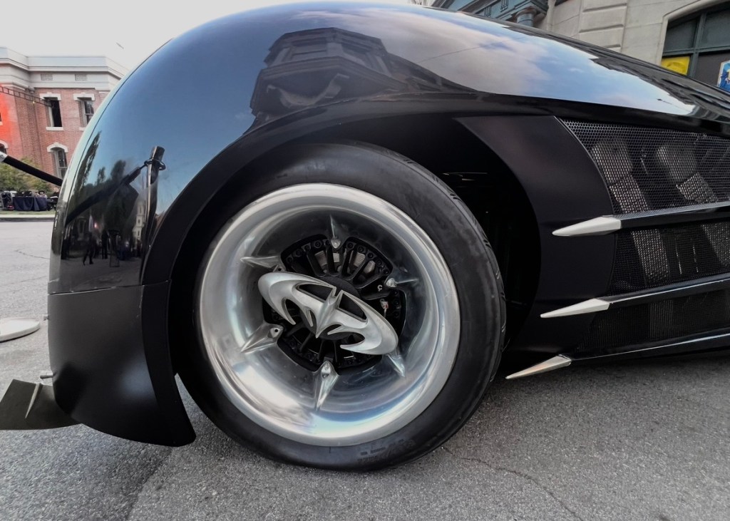 Close-up view of a sleek black car's wheel and tire, showcasing detailed rim design and aerodynamic elements.