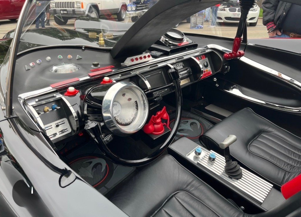 Interior view of a classic car featuring a futuristic dashboard, sleek steering wheel, and black leather seats.