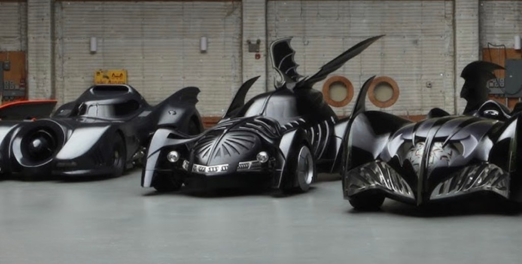 A display of three iconic black Batman vehicles, showcasing distinct designs and features, set against a spacious industrial background.