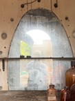Interior view through an arched window with a blurred reflection in the glass, framed by an aged wall and bottles in the foreground.