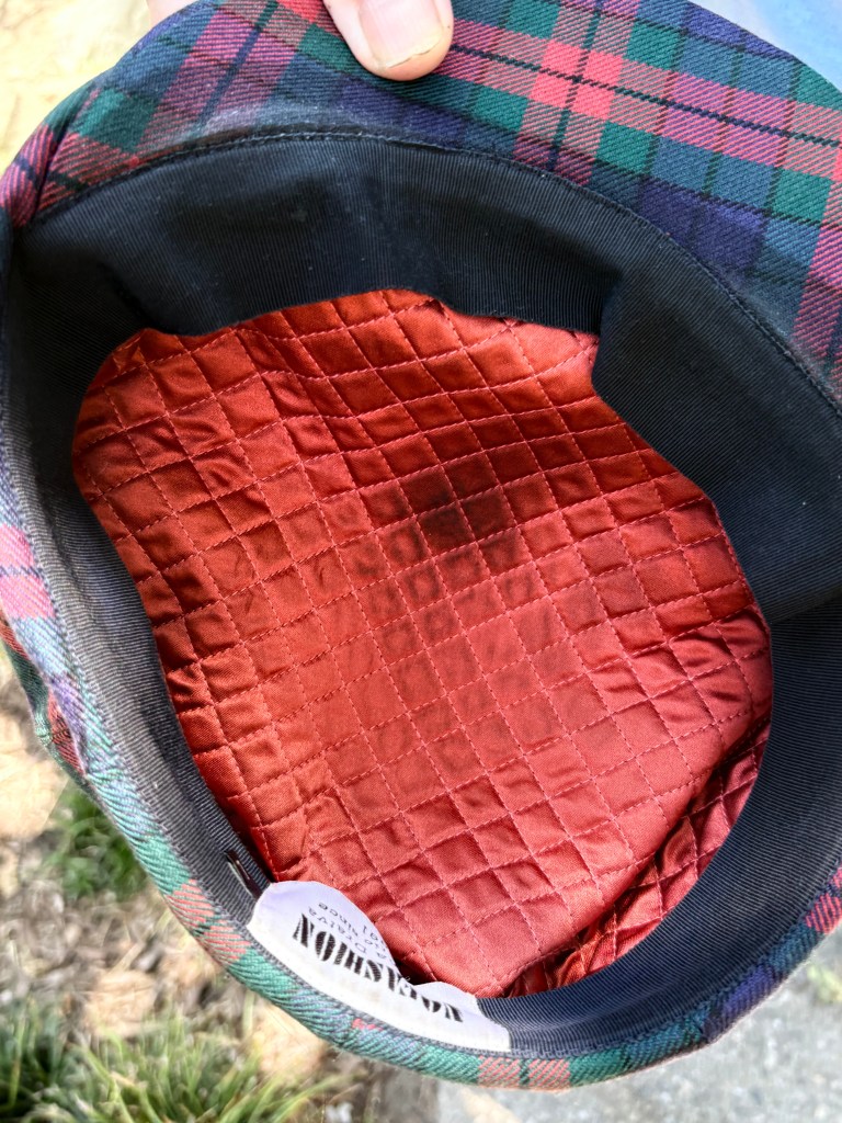 Interior of a hat featuring a plaid pattern and a quilted red lining, with a label visible at the edge.