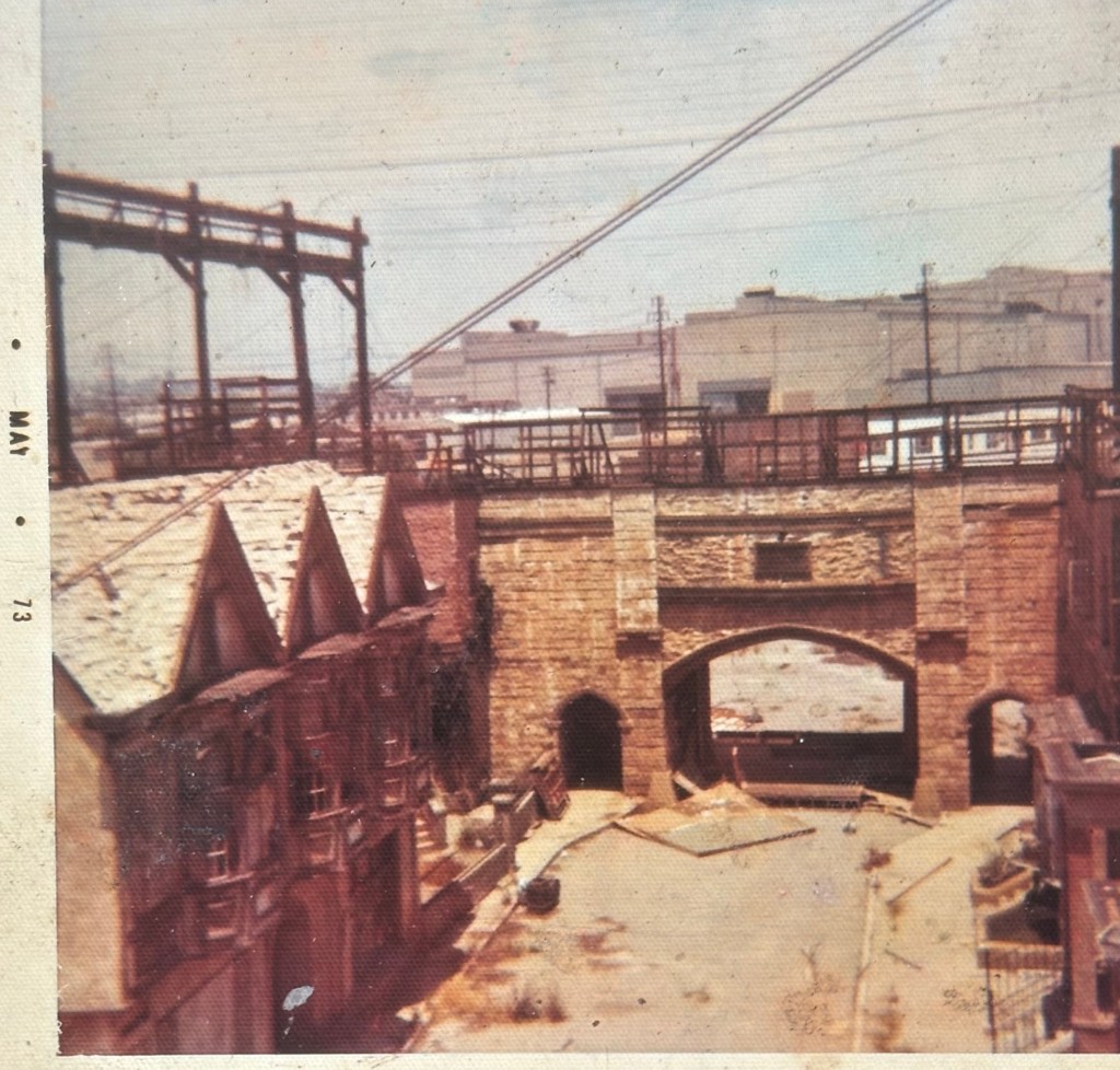 A vintage photograph showing a stone bridge with arches, surrounded by wooden structures and construction elements in an open area.