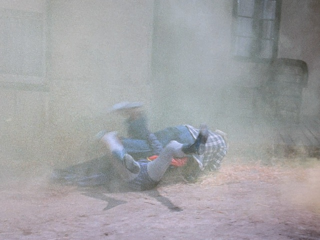 Two figures rolling on the ground amidst dust and debris, partially obscured by smoke.