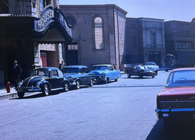 A vintage street scene showcasing several classic cars parked along a city street, with a historic building in the background.