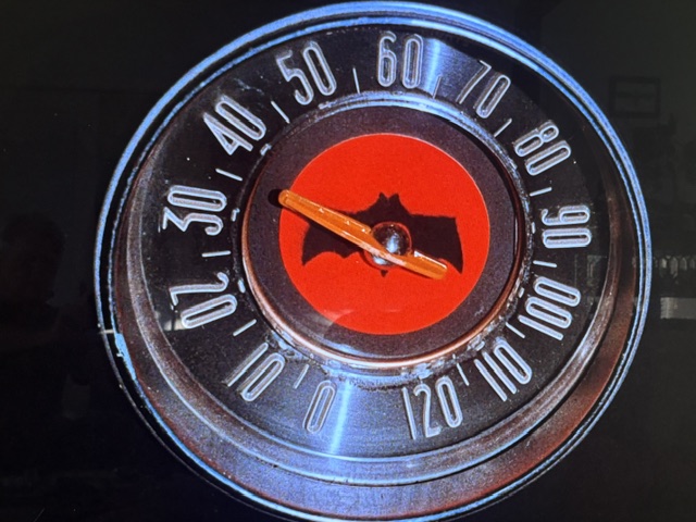 A close-up of a vintage speedometer featuring a red background with a bat silhouette and numerical speed markers ranging from 0 to 120.