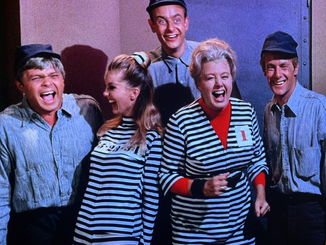 A group of five people laughing and having fun, wearing striped outfits and casual clothing, set in a colorful environment.