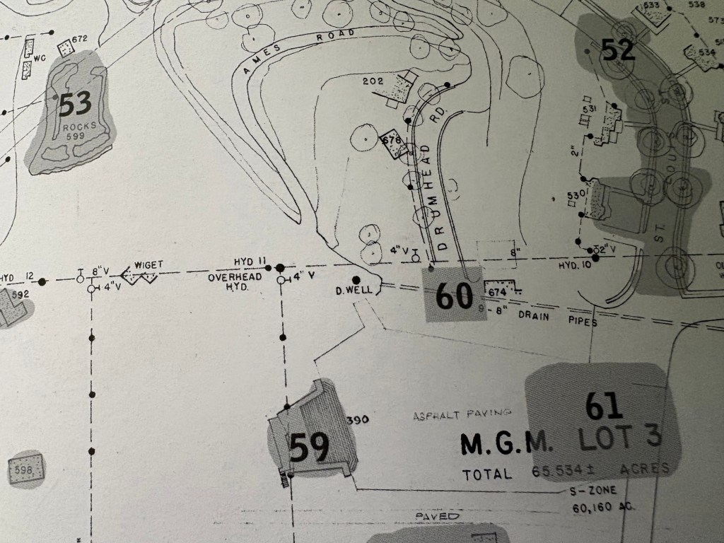 A detailed land survey map displaying various lots, structures, and roadways, including labeled sections such as 'M.G.M. LOT 3' and 'D. WELL'. The map features marked drainage pipes, hydrants, and topographical elements.