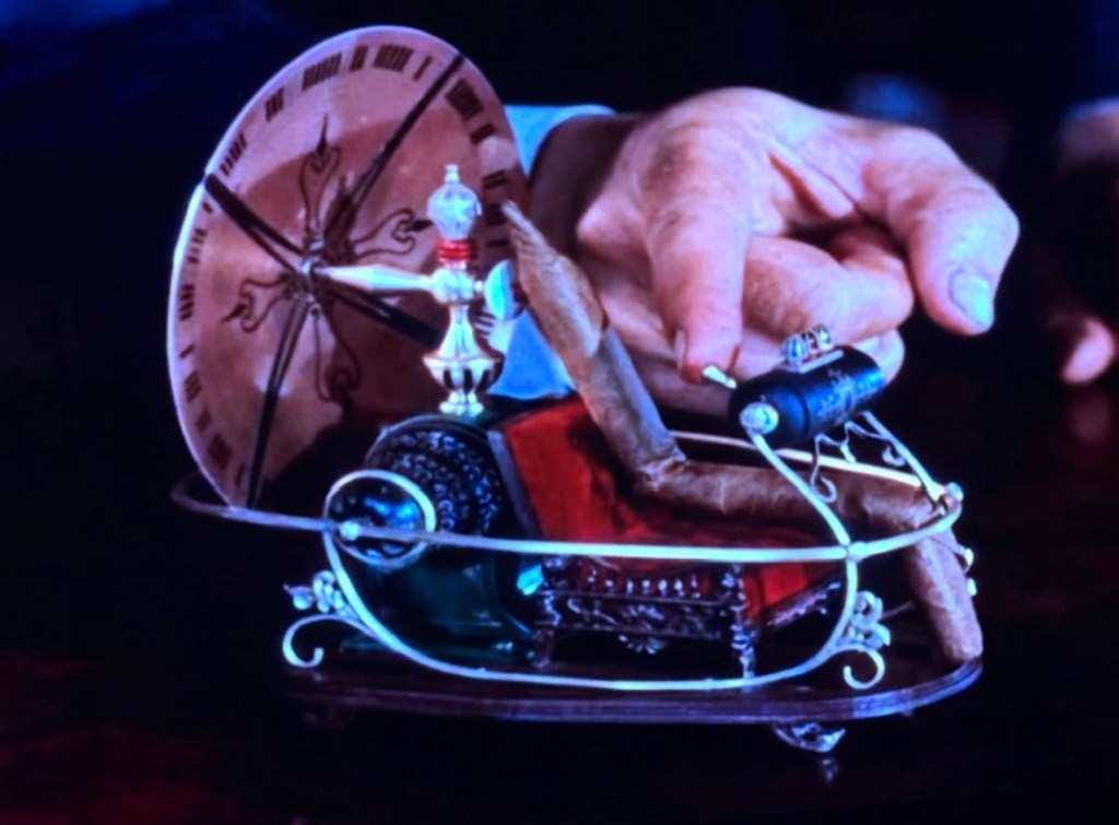 A hand holding a small, intricately designed toy vehicle with a large wheel, decorated with various components including a cigar and colorful embellishments.