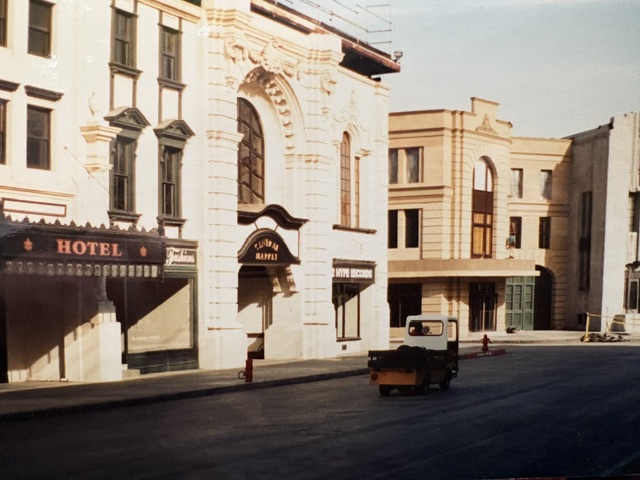A street scene featuring historical buildings, including a hotel, with a small vehicle parked on the road.