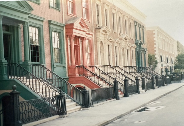A row of colorful townhouses with ornate facades and wrought iron railings, featuring steps leading to the front entrances.