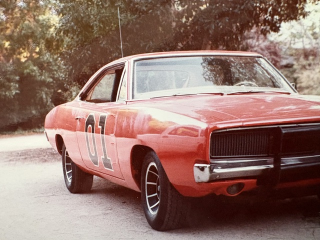 A classic red Dodge Charger car with the number '01' on the side, parked outdoors with trees in the background.