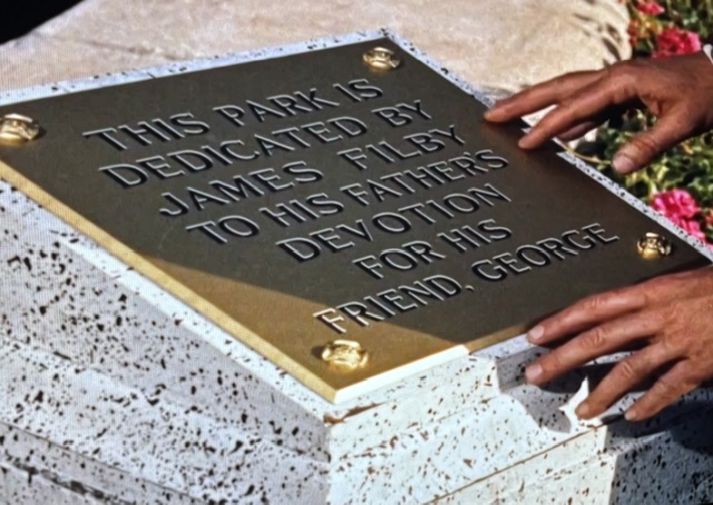 A metal plaque on a stone surface with engraved text dedicating a park to George, by James Filby, in honor of his father's devotion.