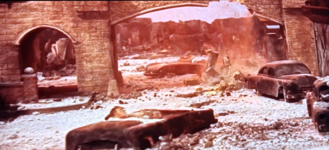 A desolate scene depicting a ruined city with destroyed buildings and abandoned cars, covered in debris and dust.