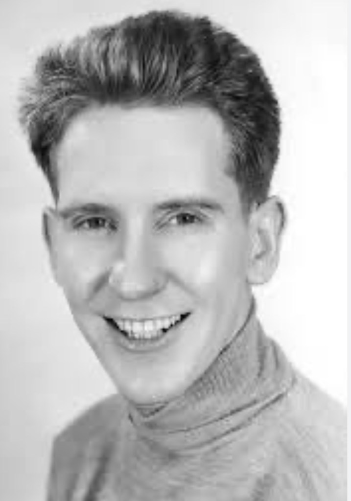 A black and white photo of a young man smiling, wearing a turtleneck sweater.