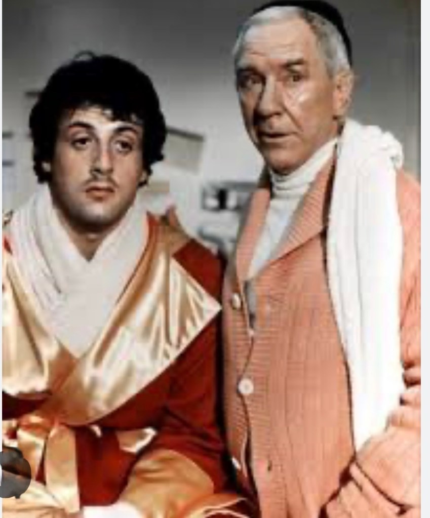 Two male characters in colorful robes, one in gold and red and the other in pink, standing together indoors with a serious expression.