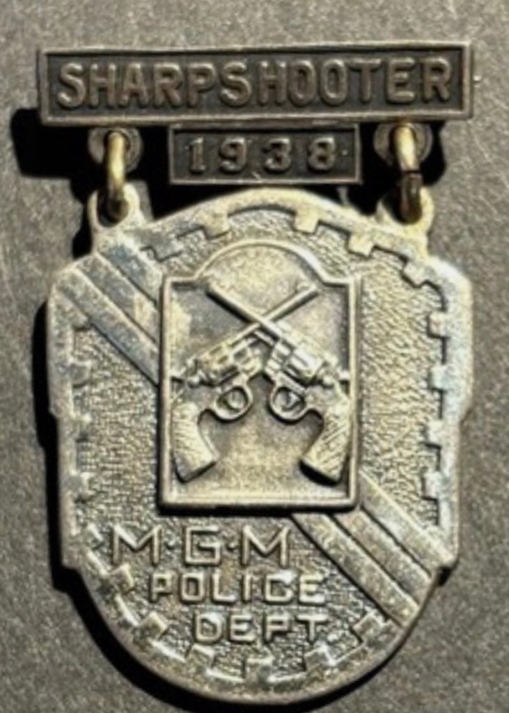 A vintage police sharpshooter medal from 1938, featuring crossed guns and the inscription 'MGM POLICE DEPT'.