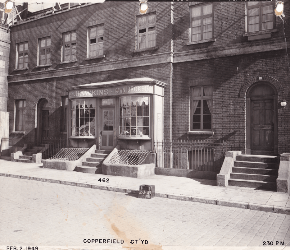Historic black and white photograph of a pawn shop named 'Hawkins Pawnbroker' featured on a street with brick buildings, benches, and steps, taken in Copperfield on February 2, 1949.