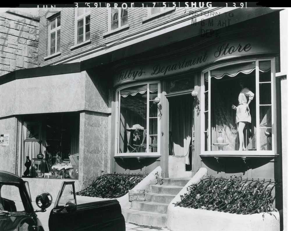 Exterior view of Gilby's Department Store featuring large windows with a mannequin display, steps leading to the entrance, and a vintage car parked nearby.