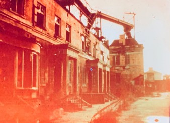 An old, faded photograph of a dilapidated building facade, with remnants of architectural features visible. The scene is tinted with a reddish hue, showing signs of neglect and decay.
