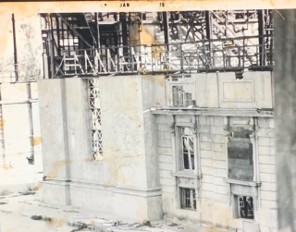 A black and white image showing a partially constructed building with scaffolding and exposed structural elements. Some windows and architectural details are visible on the facade.