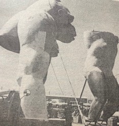 Two large, unfinished statue prototypes of gorillas displayed outdoors, with a visible construction area and vehicles in the background.