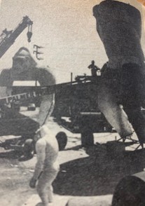 A black and white photo of a construction site featuring large machinery and equipment, with workers in protective gear present.