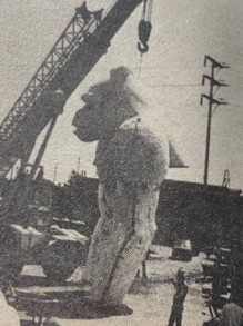A large statue of a gorilla being lifted by a crane at a construction site, with workers observing.