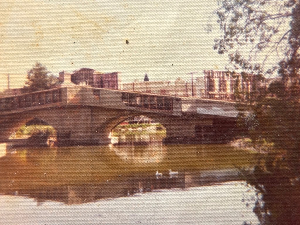 A bridge spanning a calm river, with reflections visible in the water and trees lining the banks.
